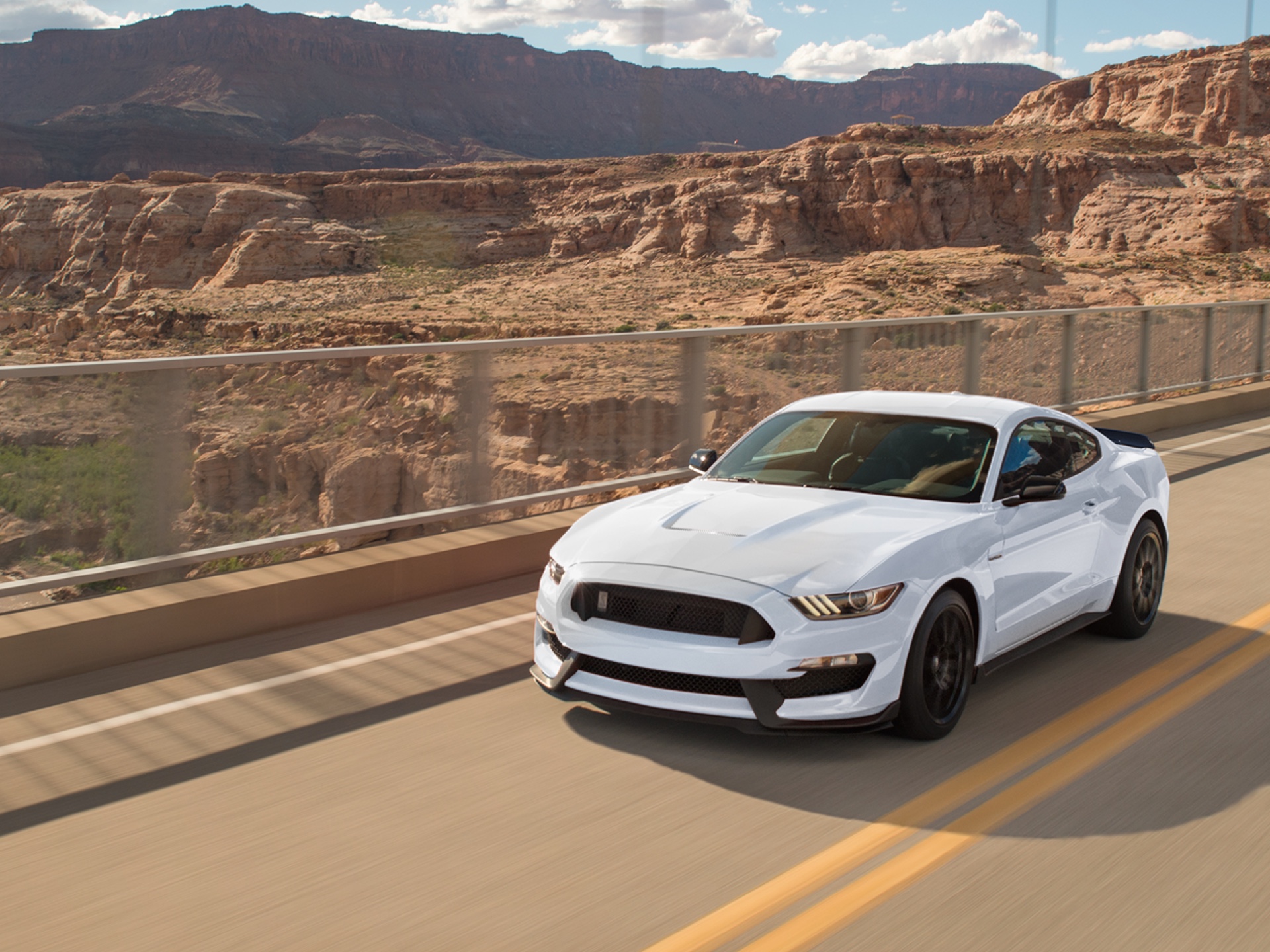 White Mustang Shelby GT350 with blue racing stripes driving through a desert landscape